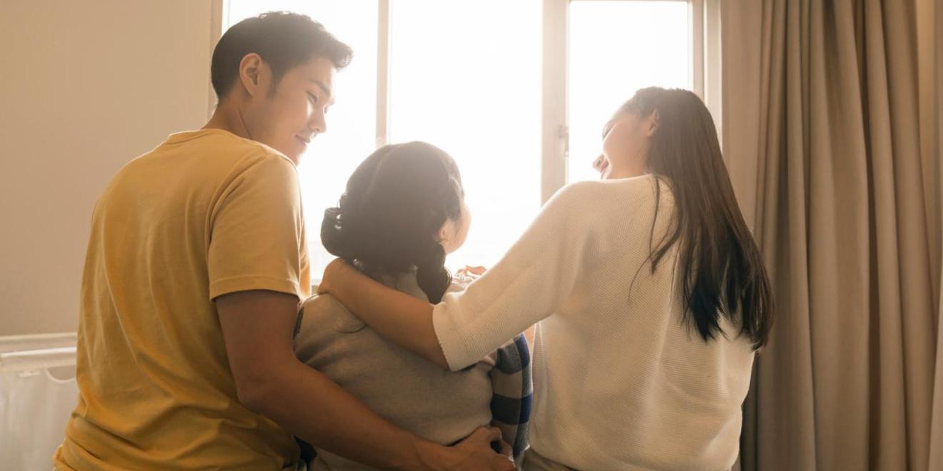 Family sitting in group with morning sunlight flare from window on bed